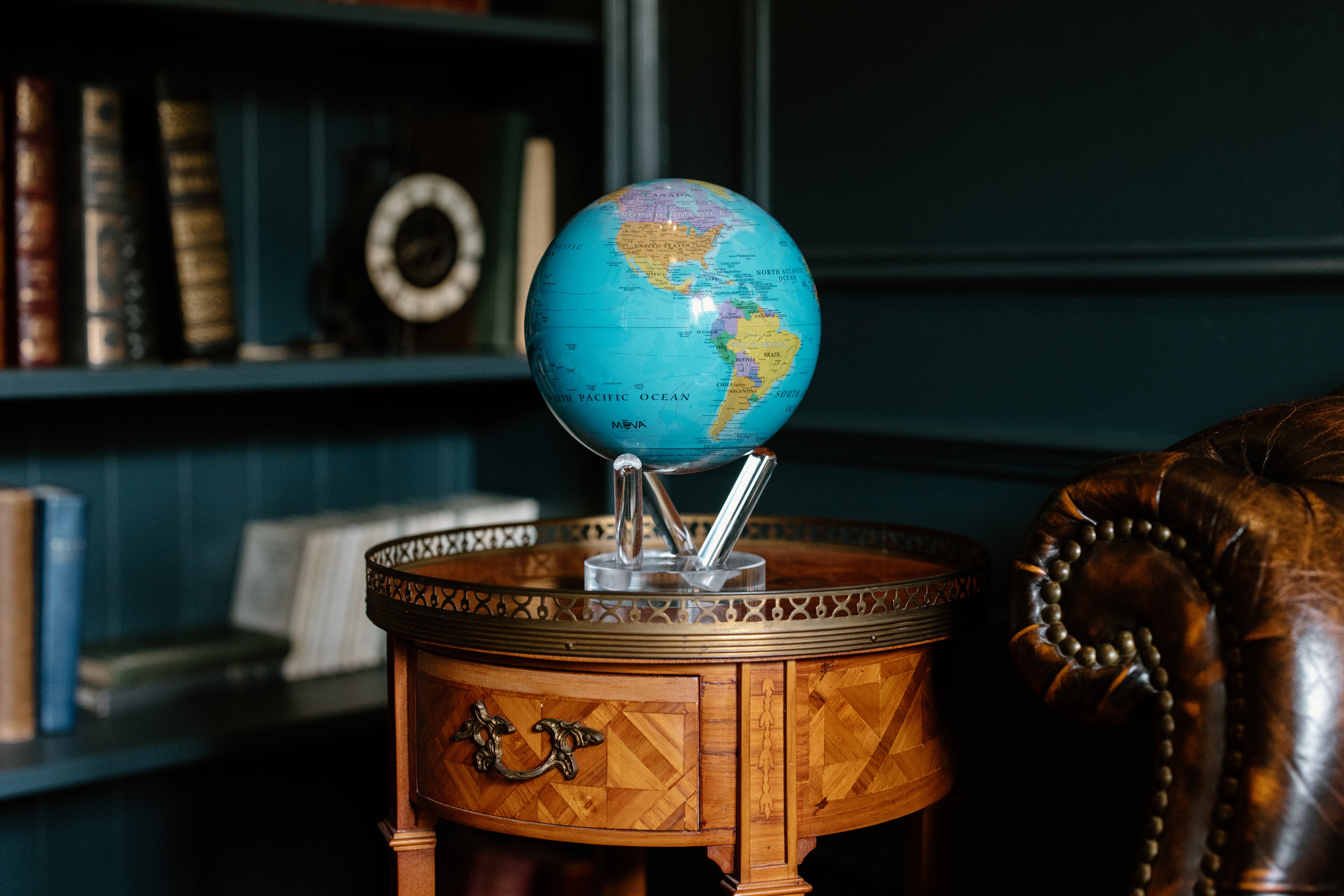 Blue political map MOVA globe with acrylic base displayed on a vintage wooden side table in a dark classic library interior