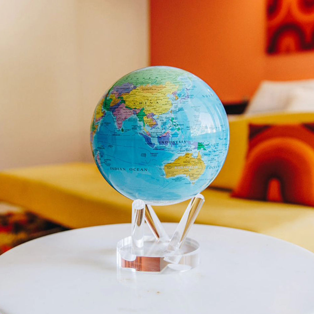 Blue political MOVA globe with acrylic base displayed on a white table in a colorful modern interior