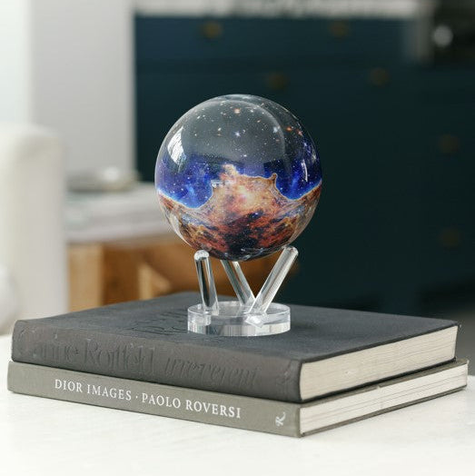 A stunning MOVA Globe featuring the James Webb Telescope’s vivid Carina Nebula image, displayed on a sleek clear stand atop two books.