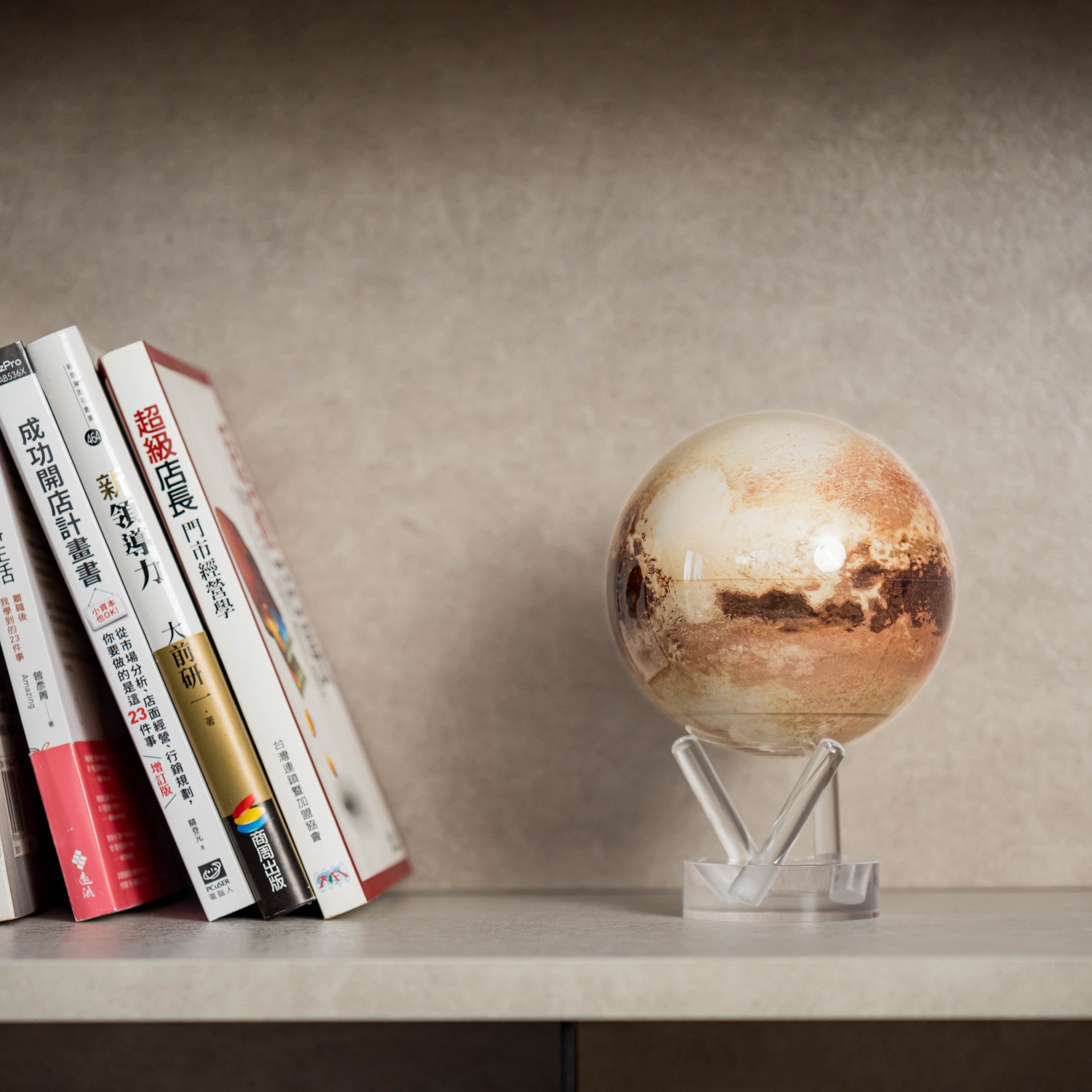Pluto MOVA Globe displayed on bookshelf with books and clear acrylic base