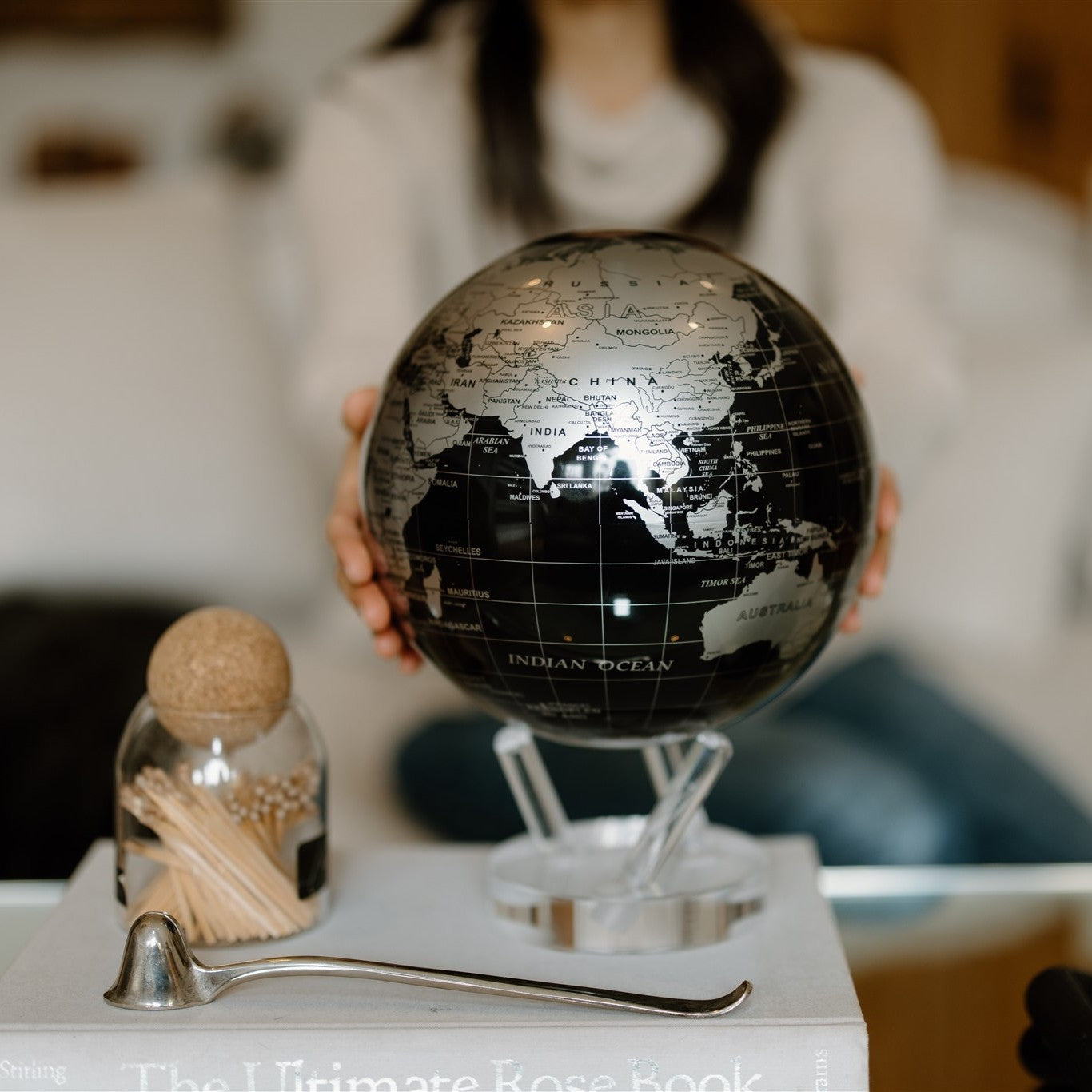Jet Black & Silver MOVA Globe displayed on book with hands in background