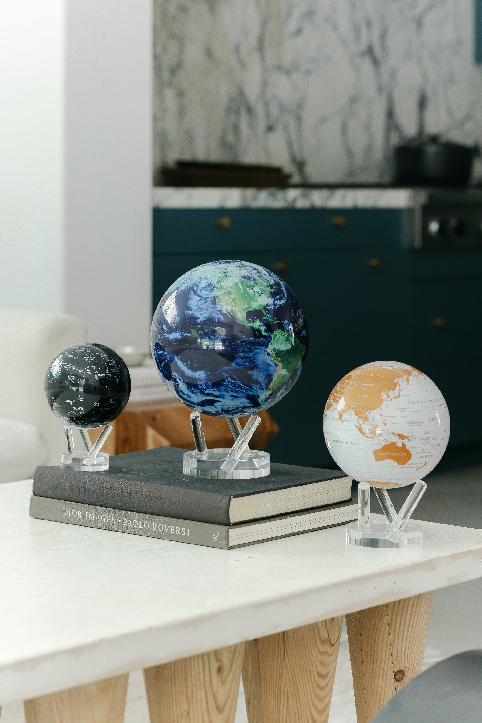 Collection of MOVA globes with acrylic bases styled on books in a modern kitchen interior