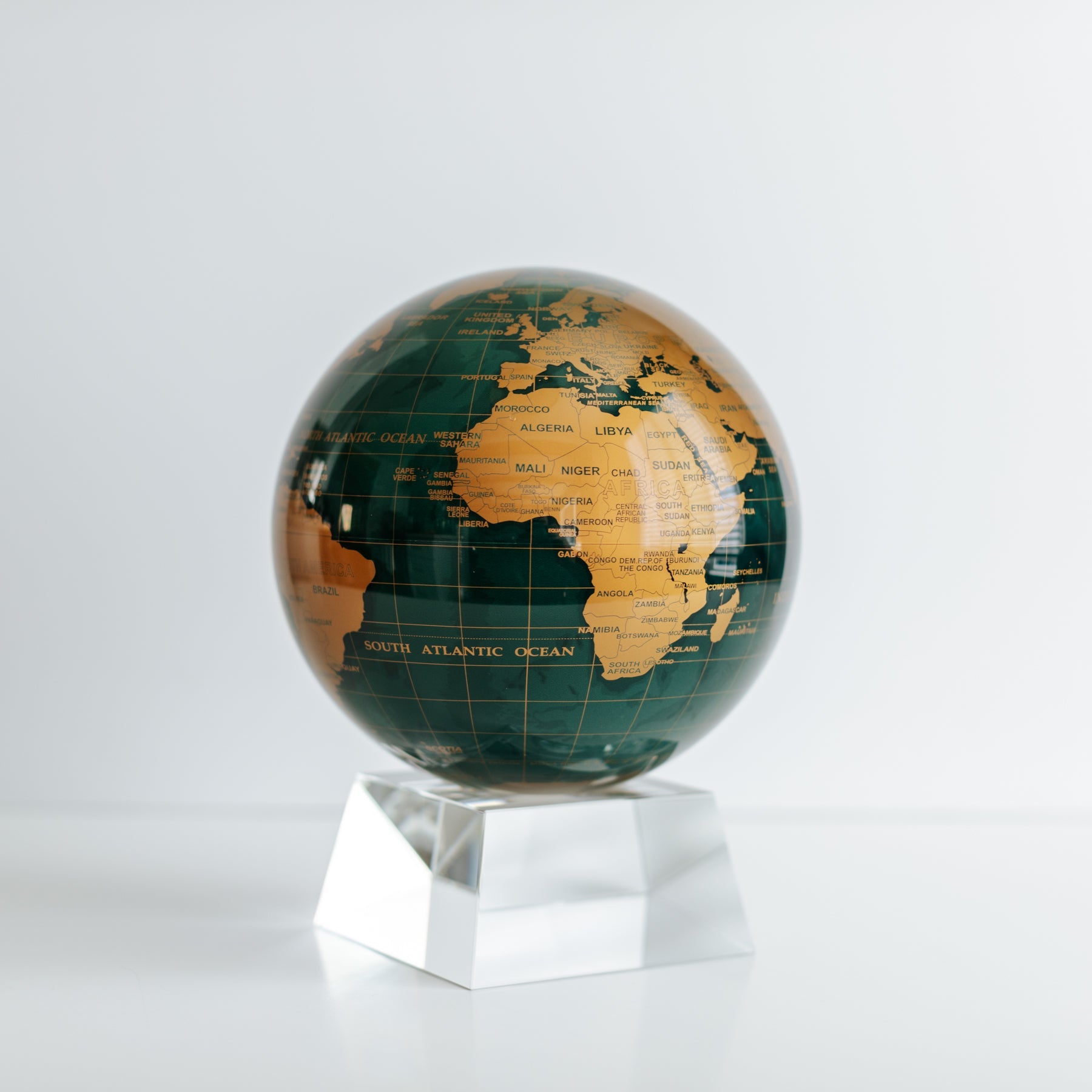 Close-up of Green and Gold MOVA rotating globe on crystal base, contemporary desk ornament and sophisticated gift"