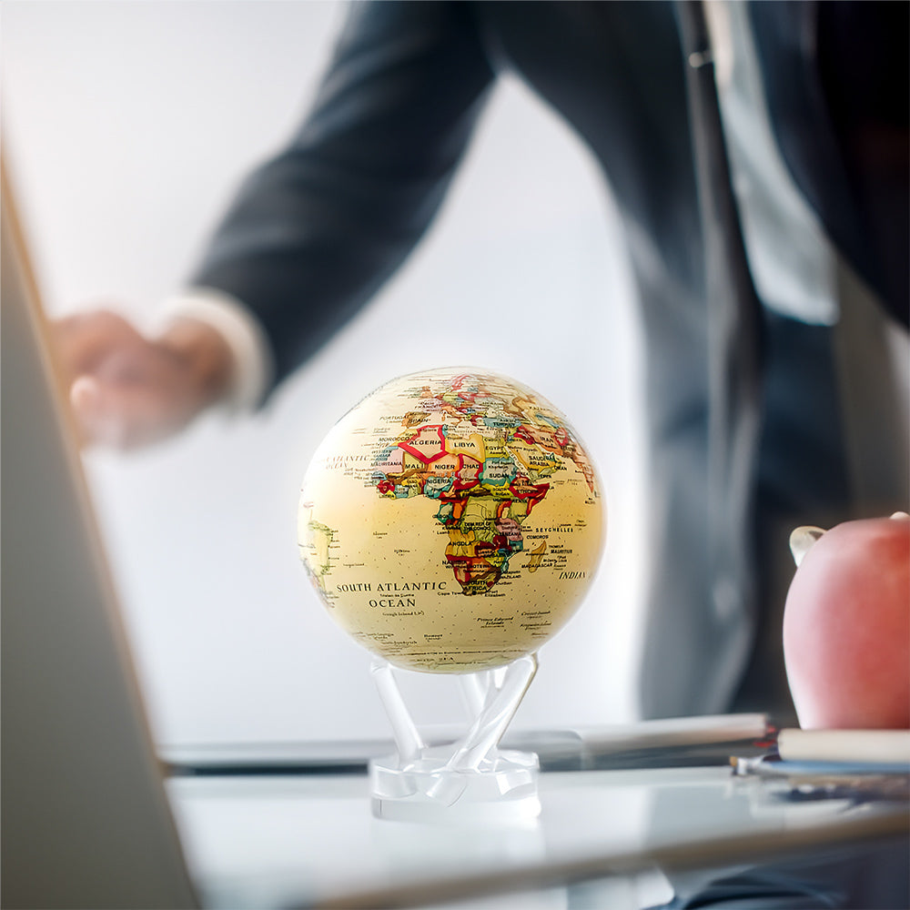 Antique political map MOVA globe with acrylic base displayed on a modern office desk beside a laptop and apple