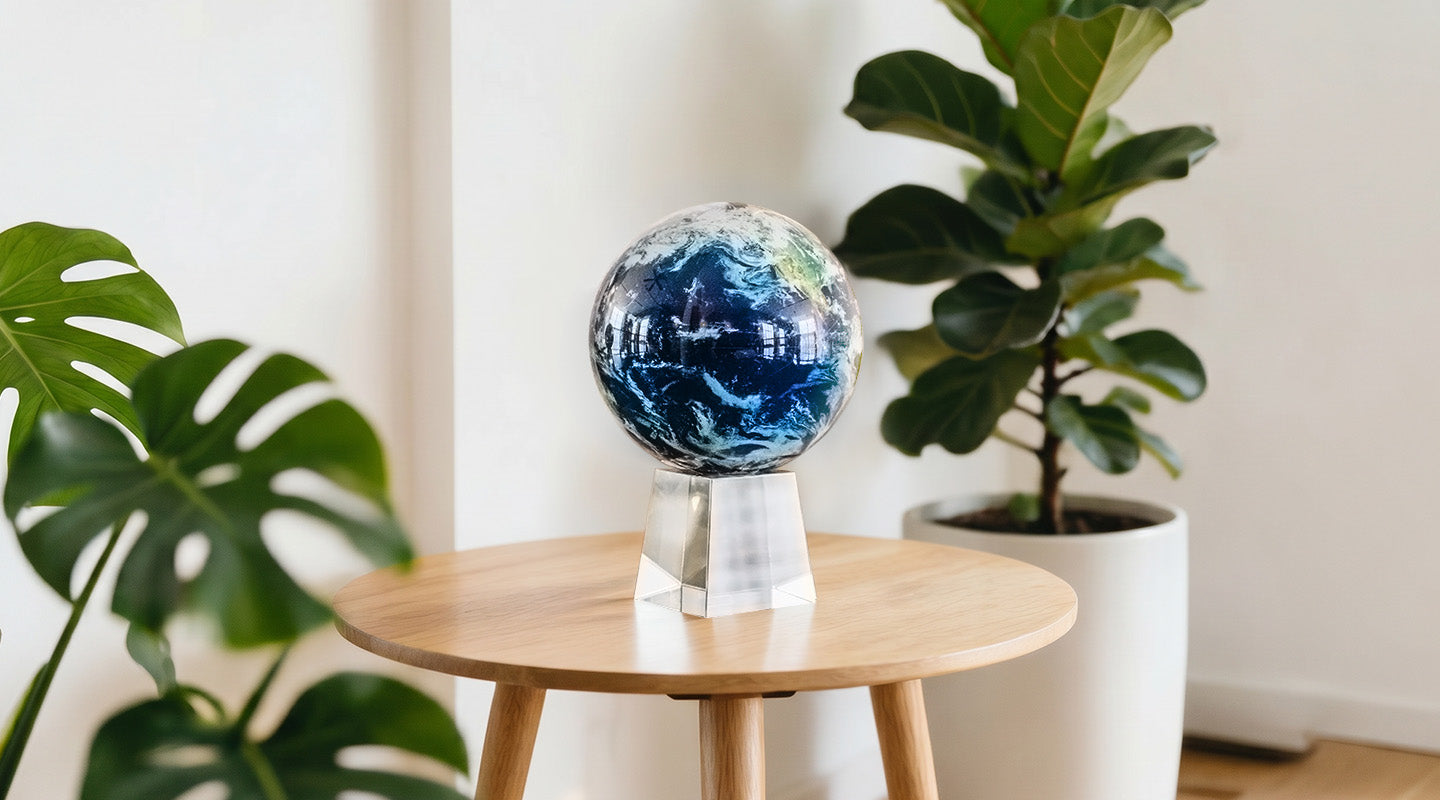 MOVA Earth with clouds globe displayed on crystal base atop side table with lush indoor plants and modern decor