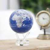 Royal Blue & Silver MOVA Globe beside a vintage clock on a wooden tabletop