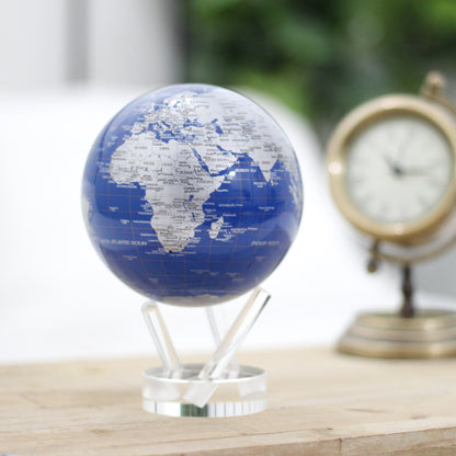 Royal Blue &amp; Silver MOVA Globe beside a vintage clock on a wooden tabletop