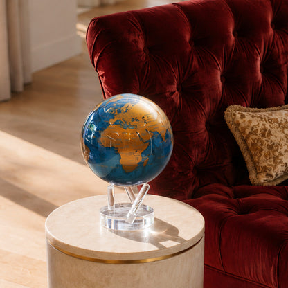 Cerulean Blue &amp; Gold MOVA Globe on base styled beside a velvet armchair in a modern luxury interior.