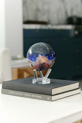 A stunning MOVA Globe featuring the James Webb Telescope’s vivid Carina Nebula image, displayed on a sleek clear stand atop two  books. 