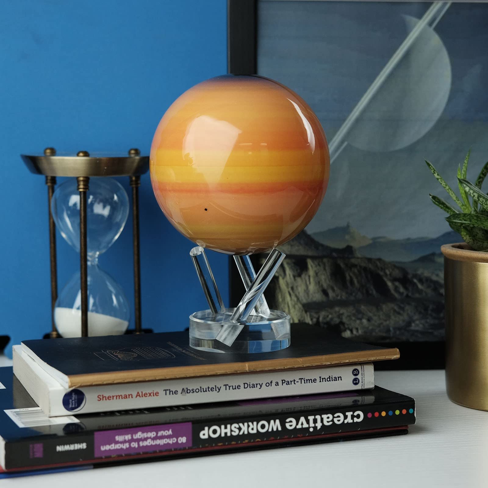 Saturn MOVA Globe displayed on bookshelf with hourglass and books