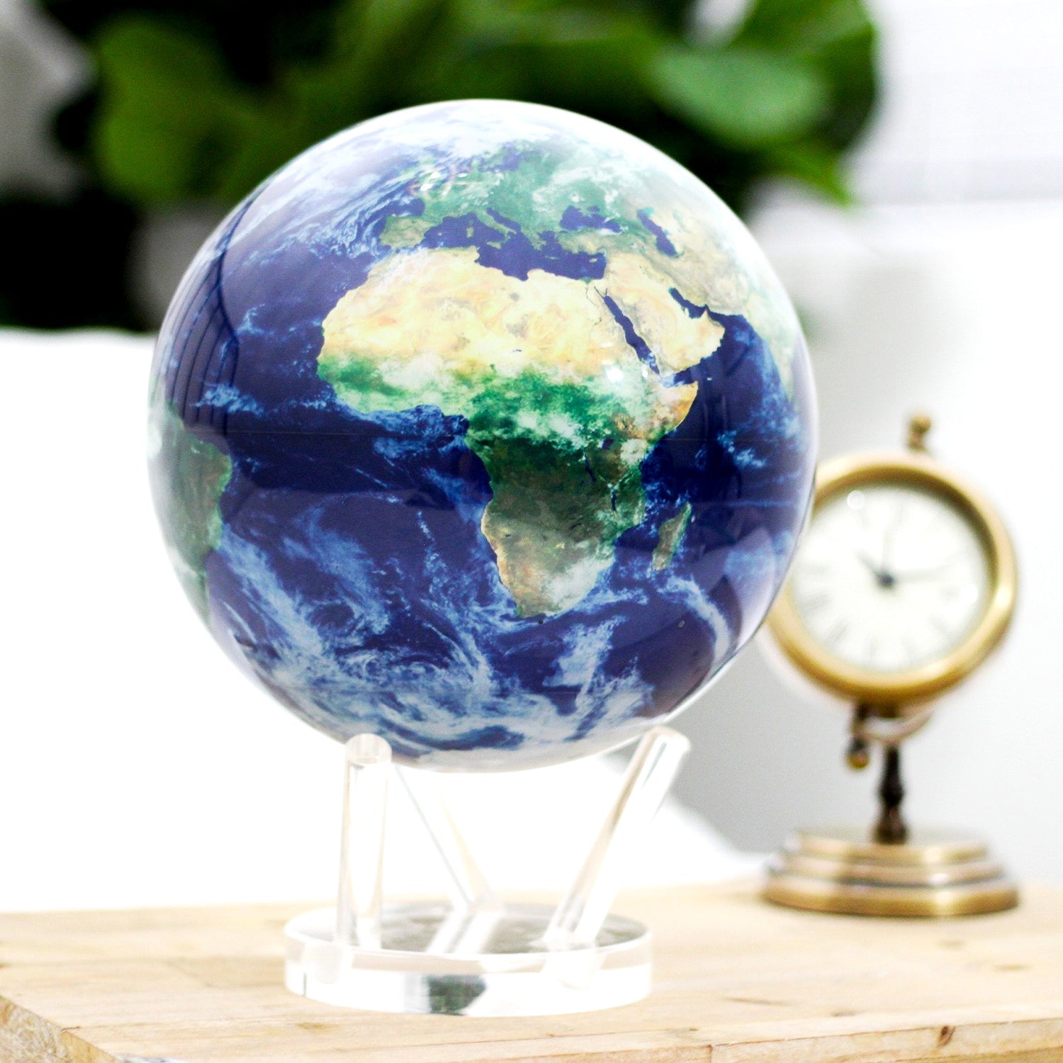 Earth with Clouds MOVA Globe on acrylic stand beside vintage clock, perfect for study or office art piece