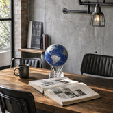 Royal Blue & Silver MOVA Globe on a wooden desk beside an open book in a contemporary office