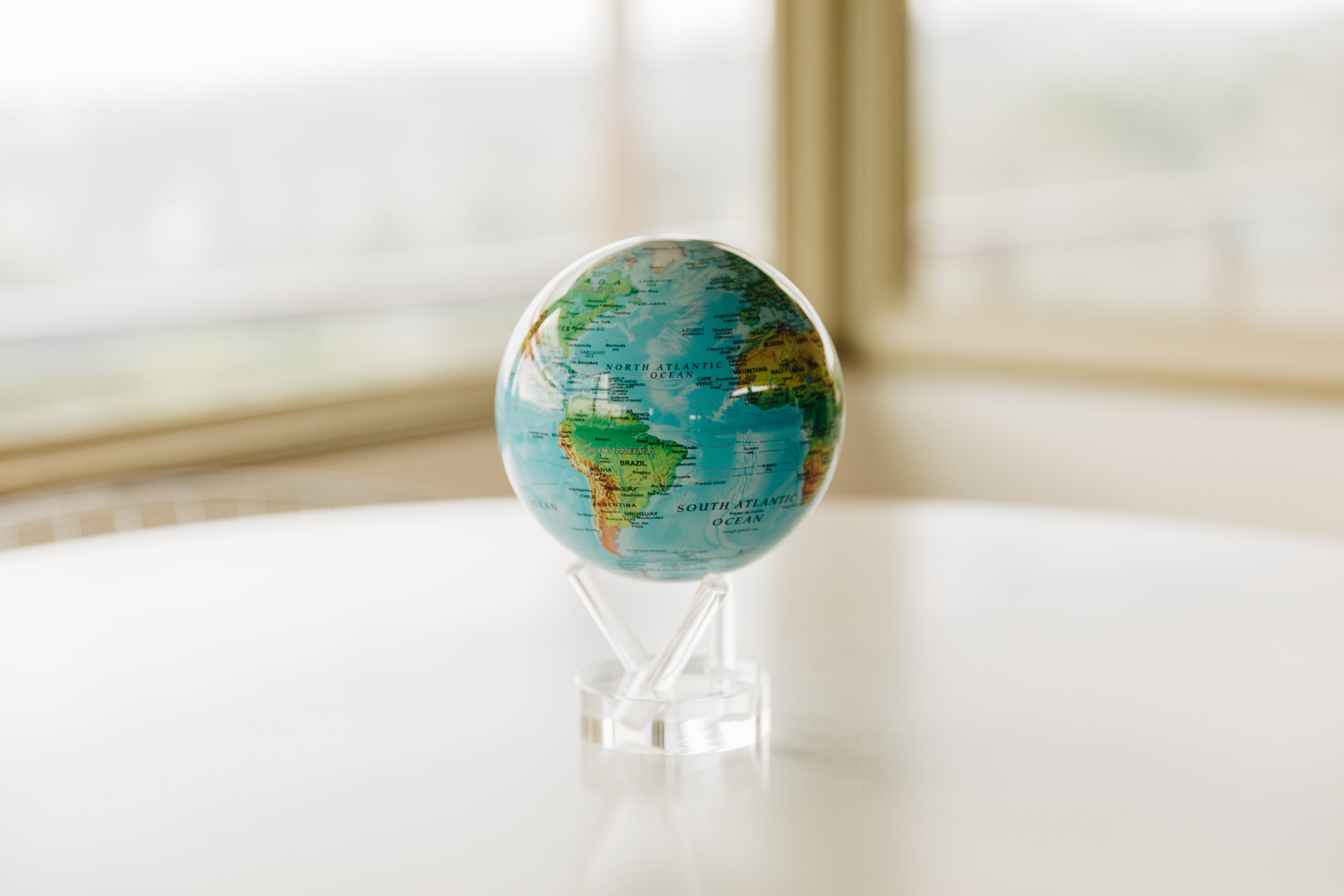 Blue political map MOVA globe with acrylic base on a white table in a bright minimalist interior near a window