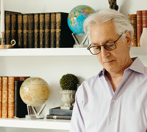 Retired man reading beside MOVA globes and vintage bookshelves in warm classic home library setting
