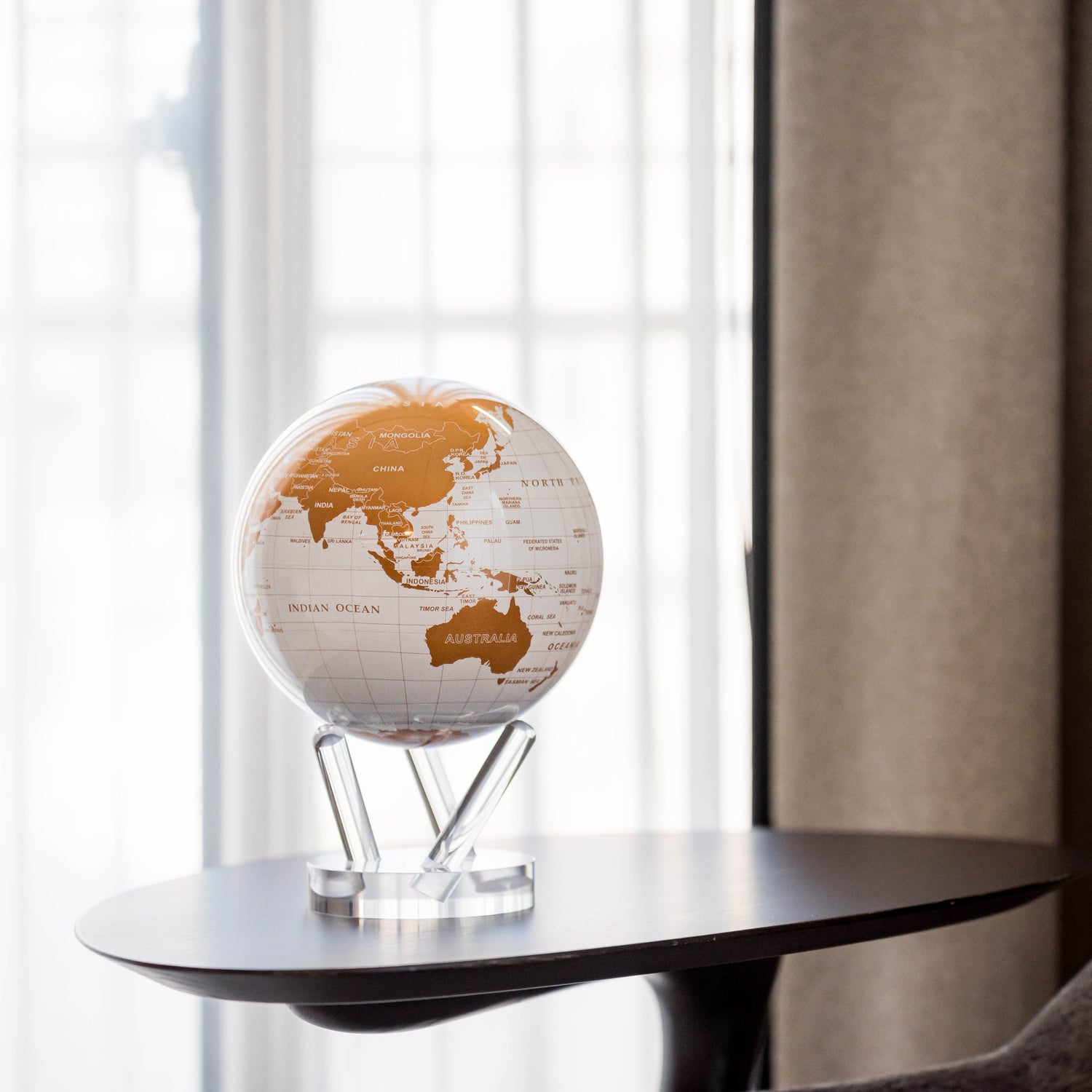 Pearl White &amp; Gold MOVA Globe with acrylic base displayed by a sunlit window in a modern living room